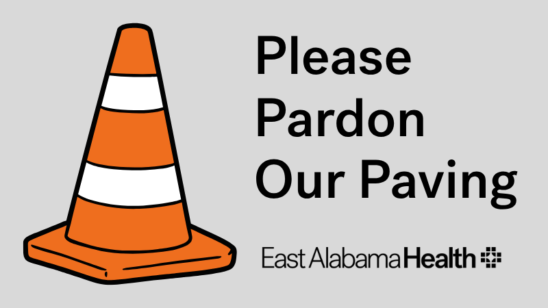 A traffic cone next to a text containing "Please pardon our Paving"