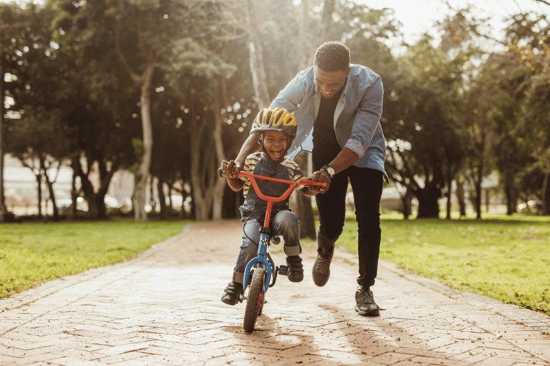 A father helping a son ride a bicycle.