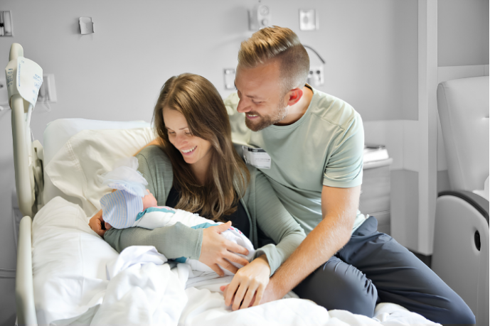 A man and woman looking happily at their newborn child while in a hospital bed