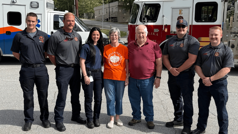 Sue McDonough and her husband standing with first responders who helped save her.