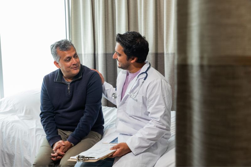 Male doctor speaking with a male patient in treatment room. 